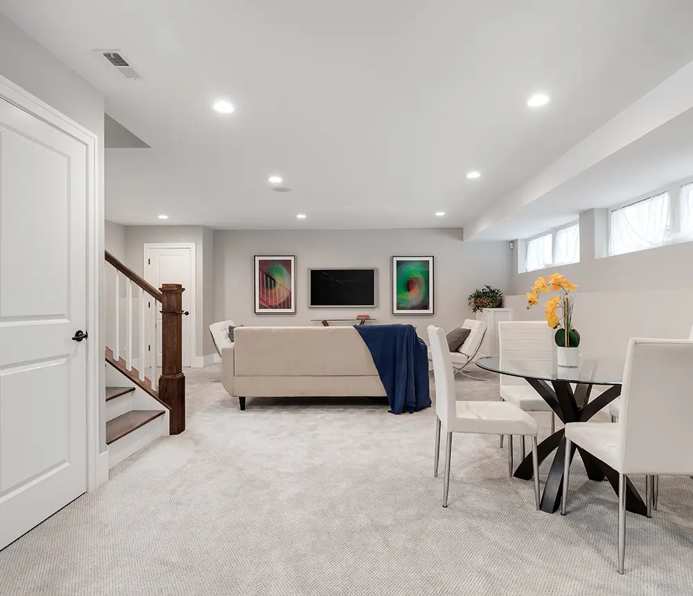 colorado white basement remodel, gray carpet floor, glass table with white chairs and cream beige sofa with TV