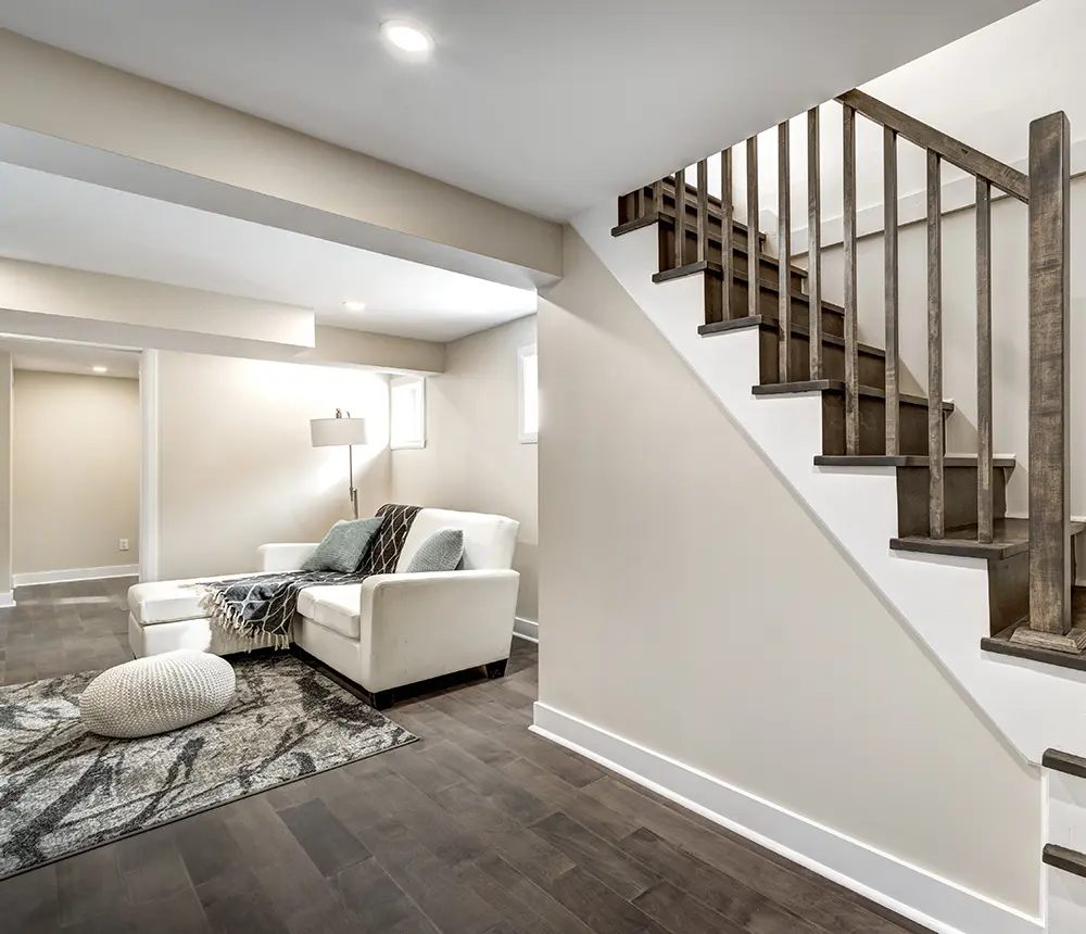 renovated basement with wood floor, white walls and sofa, wooden stairs and spotlights